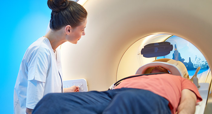 une femme regardant un homme allong&eacute; dans un scanner